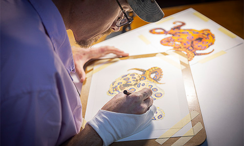 Joseph carefully placing colored droplets of ink on in his original artwork